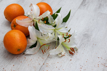 white lilies in a  glass vase and on the floor with oranges