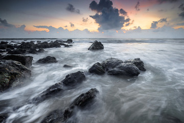 Fototapeta premium A scenery of sunrise with amazing unique rock formation and beautiful flow of wave at Kemasik beach, Terangganu Malaysia. Soft focus during long exposure shot.