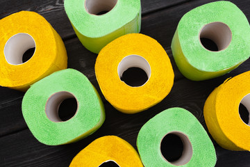 Green and yellow toilet paper rolls on dark wooden background top view