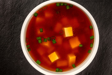 A closeup of miso shiru soup with tofu and scallions, shot from the top on a black background