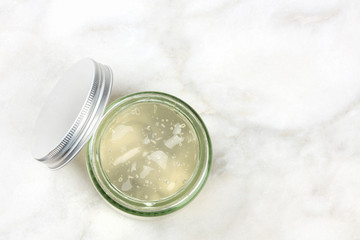A glass jar with aloe vera gel, shot from above on a white marble background with copy space
