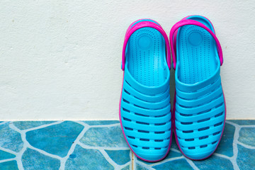 Blue sandals with ankle straps placed on a white wall.