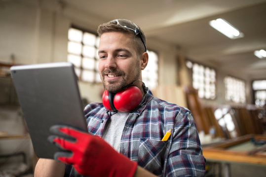 Portrait of middle aged professional worker carpenter with ear protectors using tablet in carpentry workshop. Talented and creative people. - Powered by Adobe