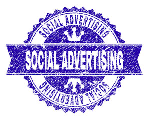 SOCIAL ADVERTISING rosette seal watermark with distress style. Designed with round rosette, ribbon and small crowns. Blue vector rubber watermark of SOCIAL ADVERTISING label with scratched texture.