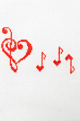 Musical heart and notes are embroidered with red threads on white fabric.