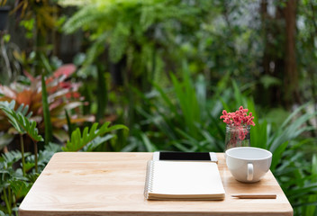 Workspace outdoors with memo notebook,pencil,white coffee cup,mobile phone andd beautiful vase green nature background