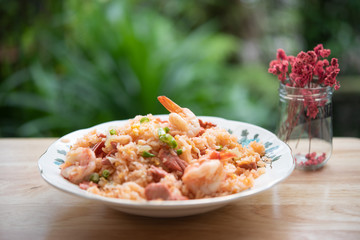 Delicious Thai fried rice with shrimp on wooden table with beauitful vase ,green blurred background