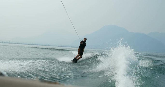 Front view of caucasian young man doing tricks on wakeboard in the city river 4k