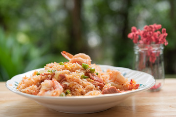 Delicious Thai fried rice with shrimp on wooden table with beauitful vase ,green blurred background