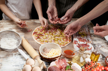 Obraz na płótnie Canvas Hands of mom and her children to cook delicious pizza with prosciutto, vegetables and cherry tomatoes. Close-up