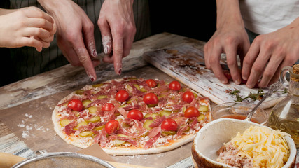 Horizontal Food Banner. Mom and her children prepare delicious homemade pizza with prosciutto and vegetables in the kitchen. Hands of people close up