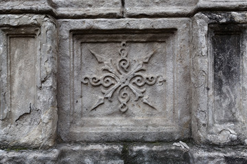 Close-up: a stone element of an old ornament on a crumbling wall with cracks in an ancient temple