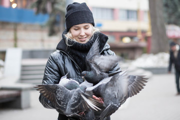 Birds doves eat sunflower seeds from the hands of a beautiful young girl in a black jacket and hat...