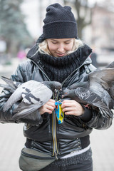 Birds doves eat sunflower seeds from the hands of a beautiful young girl in a black jacket and hat...