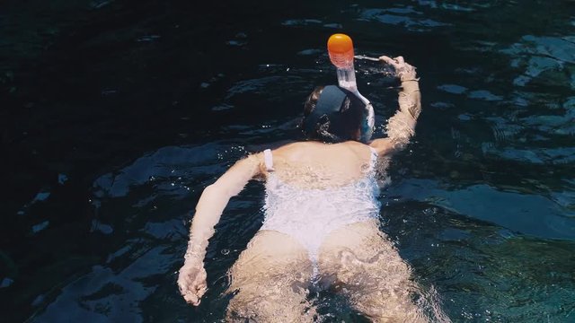 Young woman snorkeling and making underwater photo video with mobile phonee in the blue tropical water wearing white swimsuit.