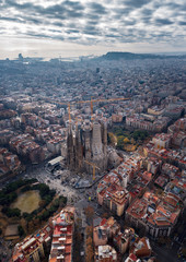 Aerial; drone view of main Gaudi project Sagrada Familia Temple; majestic building towering over the rooftops of Eixample; sharp domes and unusual forms of the great unfinished work of neo-gothic art