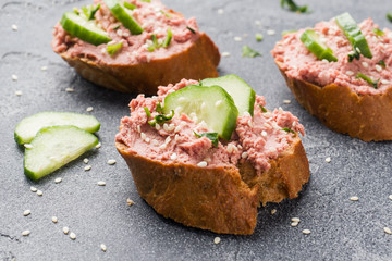 Sandwiches with chicken pate and cucumber on dark table.