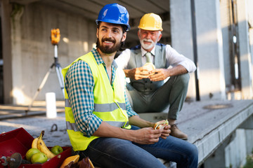 Happy young and senior engineer worker sitting at building site on break