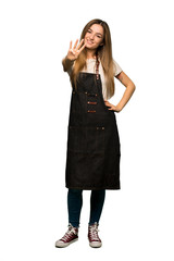 Fototapeta premium Full body Young woman with apron happy and counting four with fingers on isolated background