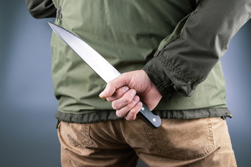 large kitchen knife behind a man in a green jacket on a gray background