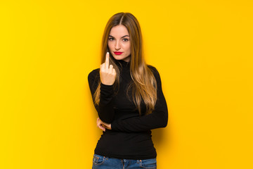 Young pretty woman over yellow background making horn gesture