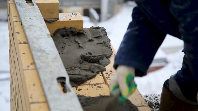 Builder is imposing building solution on a wall during doing brick masonry