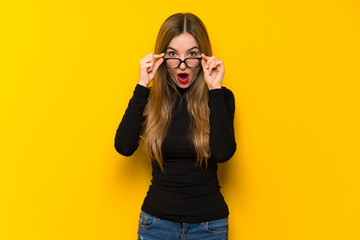 Young pretty woman over yellow background with glasses and surprised