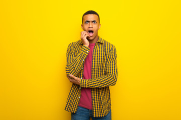 Young afro american man on yellow background surprised and shocked while looking right