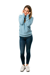 Full body of Blonde woman with blue shirt covering ears with hands. Frustrated expression on white...