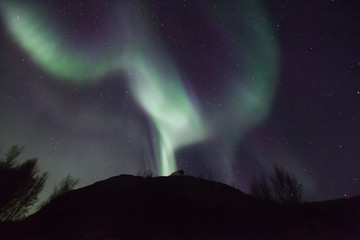 northern lights in Norway in green, blue and violet colours and a silhouette  of a mountains in front