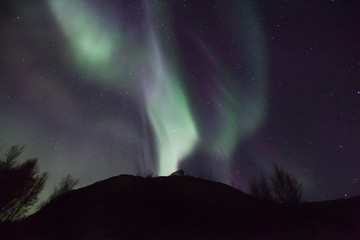 northern lights in Norway in green, blue and violet colours and a silhouette  of a mountains in front