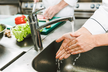 cropped view of female chef washing hands over sink in restaurant kitchen