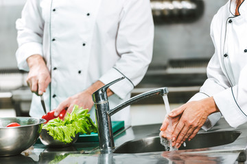 cropped view of female chef washing hands over sink while colleague cooking on background in restaurant kitchen