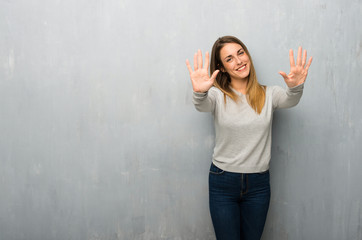 Young woman on textured wall counting ten with fingers