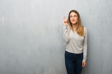 Young woman on textured wall with fingers crossing and wishing the best