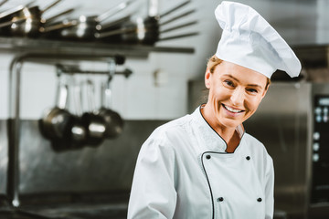 beautiful female chef in uniform and hat looking at camera in restaurant kitchen with copy space