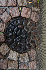 Scandinavian manhole in its urban surrounding.  Hidden beauty in design, texture, colors, shape and pattern of a sewer cover 