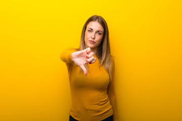 Young woman on yellow background showing thumb down sign with negative expression
