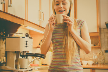 Woman in kitchen making coffee from machine