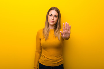 Young woman on yellow background making stop gesture denying a situation that thinks wrong