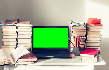 Green screen laptop, stack of books, notebooks and pencils on white table, education office concept background.