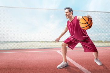 Cheerful asian basketball player man in action with the ball