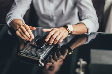 hands of a businessman holding a phone and purse on the table in the cafe. Close up