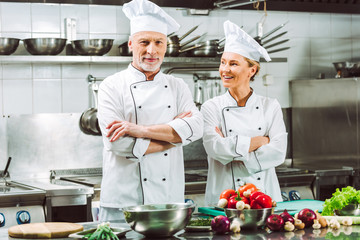 female and male chefs in uniform with arms crossed during cooking in restaurant kitchen