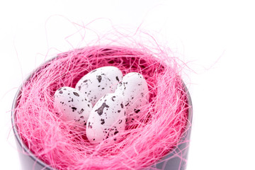 Quail eggs in pink sisal nest, metal box on white