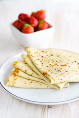 Crepes with fresh strawberries on a white porcelain plate. White wooden table, high resolution