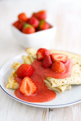 Crepes with fresh strawberries and strawberry purée on a white porcelain plate. White wooden table, high resolution