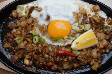 Pork sisig sizzling mince pork Filipino food with raw egg cooking hot on clay pot tray with lemon slice and fresh red chilies Asian cuisine tasty food with pepper on plate 