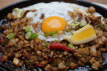 Pork sisig sizzling mince pork Filipino food with raw egg cooking hot on clay pot tray with lemon...