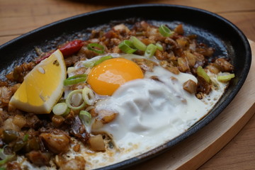 Pork sisig sizzling mince pork Filipino food with raw egg cooking hot on clay pot tray with lemon...
